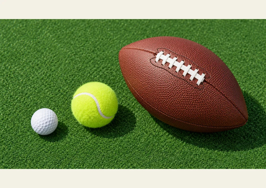 A golf ball, tennis ball and leather football arranged on green felt